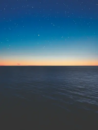 Sunset over calm ocean with starry sky