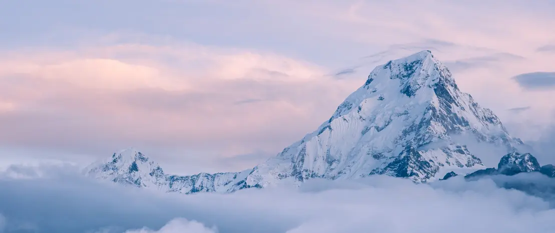 Snow-covered mountain peak above clouds at sunset