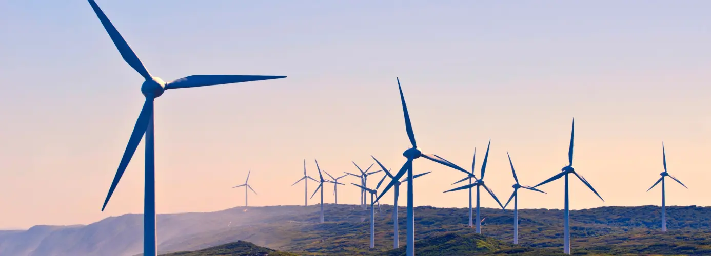 Wind turbines on a green hillside at sunset