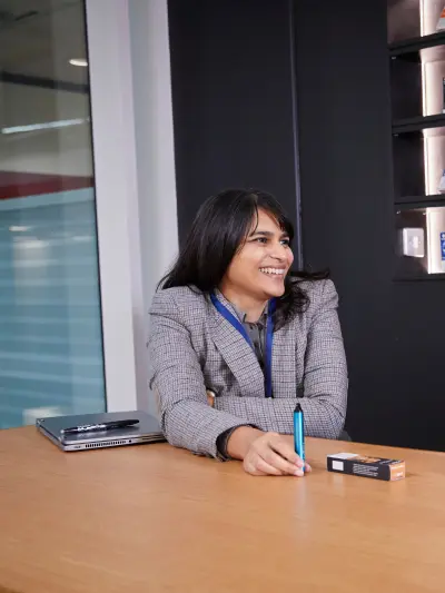 Smiling businesswoman sitting at desk in office, holding a Vuse GO device