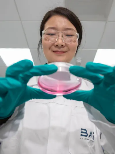 Scientist in protective gear holding petri dish with pink substance