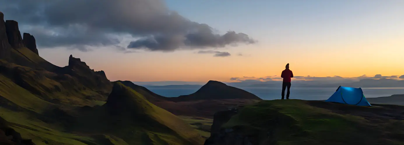Silhouette of person standing on cliff edge with tent at sunset