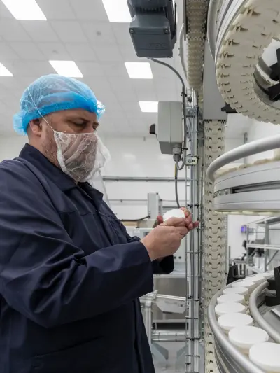 Factory worker in protective gear inspecting products on conveyor belt.