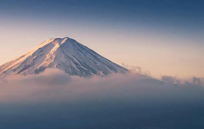 Snow-capped Mount Fuji rising above clouds at sunrise