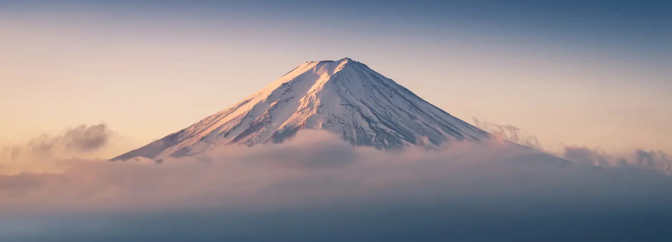 Snow-capped Mount Fuji against a pastel sky at sunrise.