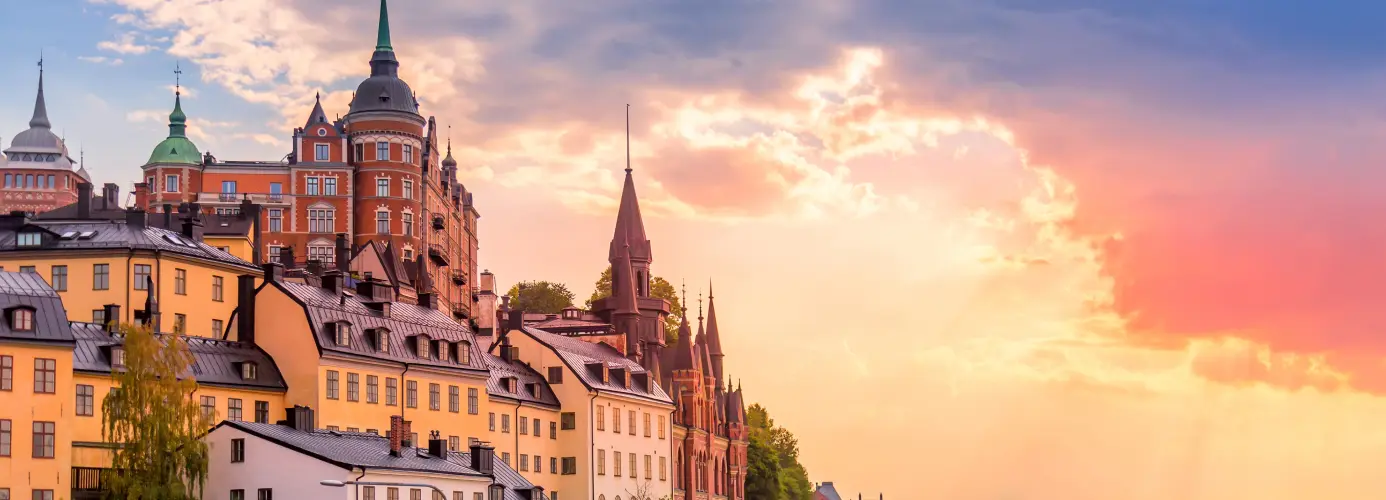 Scenic view of Stockholm's old town Gamla Stan at sunset, with colorful buildings and church spires against a vibrant sky.