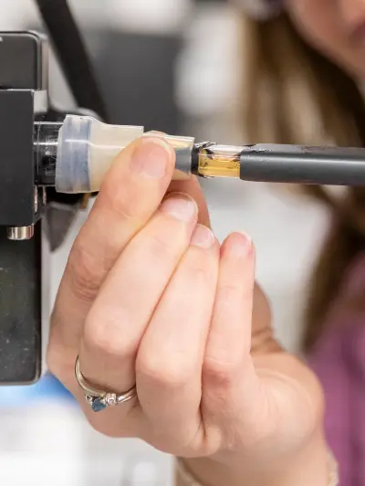 Hand inserting a Vuse device into scientific equipment, with yellow liquid visible
