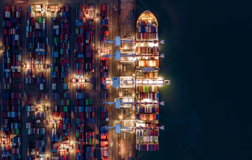 Aerial view of a container ship being loaded with colorful cargo containers at night.