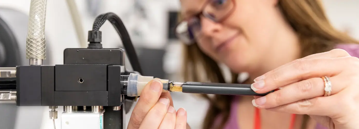 Scientist inserting a Vuse device into scientific equipment, with yellow liquid visible