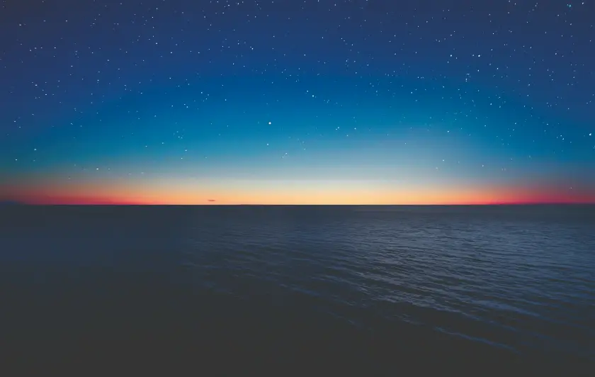 Starry night sky over calm ocean at sunset
