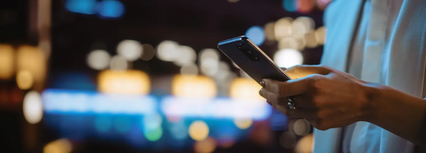 Hand holding smartphone with blurred city lights in background